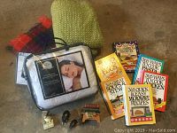 Overview of all lot items together on floor: blankets, mattress protector, cookbooks, small figurines
