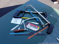 Photo showing all hacksaws and blades arranged on a table from a distance, clearly showing all items included in the lot.