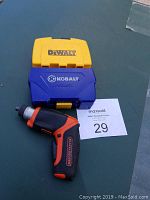 Black & Decker cordless drill with black and orange handle and two plastic cases (yellow DeWalt and blue Kobalt) closed, placed on green surface.