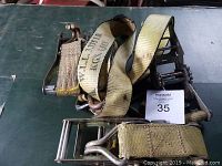 Two heavy-duty yellow ratchet straps with metal ratchet buckles and hooks, laid on a green surface.