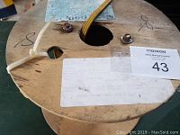 Top view of wooden spool showing yellow electric wire coming through hole and spool surface details, including marks and tag.