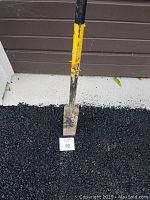 Close up of digging blade of post hole digger on asphalt showing wear and color of handle