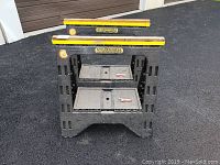 Pair of Storehorse folding sawhorses placed side by side on asphalt surface showing front view and top yellow rails.