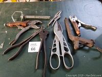 Seven vintage and used hand tools including pliers, cutters, snips, and punch, arranged on a green table.