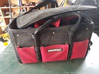 Black and red Durabuilt branded tool bag with shoulder strap and several pockets, showing good condition and ready to carry tools.