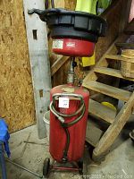Full view of red oil change drip pan on wheeled red tank with hose and valve attached.