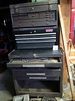 Full view of the stacked tool chests in a workshop environment showing the Craftsman toolbox on top of the Kennedy chest, one drawer of the Kennedy chest partially open with tools inside.