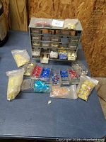 Organizer with multiple drawers filled with a variety of insulated electrical terminals and connectors, some stored inside and some loose or bagged in front of the unit.