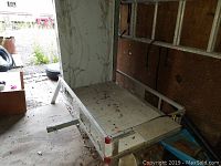 View of aluminum trailer bed with side rails, visible dirt and wear, hitch bar extended forward for towing