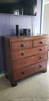 Front view of antique wooden chest showing 5 drawers with wooden knobs and keyholes.