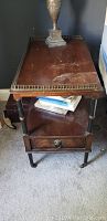 Full view of one antique wooden nightstand with brass wheel casters, showing drawer and lower shelf