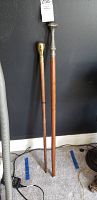 Two unique walking canes standing against a black wall, showing their full length and handles.