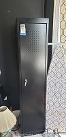 Tall black metal growlight cabinet closed, showing front door with ventilation holes and key lock.