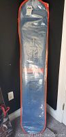 Snowboard in clear protective bag with orange trim leaning against wall