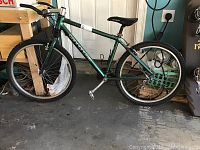 Full side view of the green Cannondale mountain bike leaning against a wall showing tires, frame and seat.