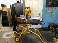 Full view of miter saw mounted on yellow wheeled stand in garage setting