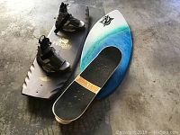 Photo of blue/white skimboard and brown wakeboard with XL boots showing wear on cement floor