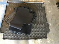 Overhead view of stacked rubber and carpet floor mats, showing textured black rubber mat on bottom and several black carpet mats on top.