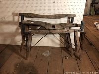 Antique wooden yoke placed on top of wooden agricultural frame against pegboard wall on wooden floor