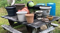 Multiple planters displayed on wooden picnic table, showing ceramic and plastic varieties