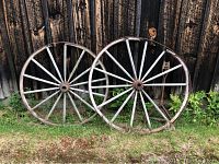 Two full antique wagon wheels against a wooden fence, showing white spokes and metal rims on grass