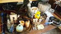 Wide view showing punch bowl set, frying pans, candles, egg cups, coins, glassware, and other kitchen and decorative items on a wooden table