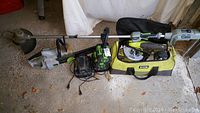 Full lot on concrete floor showing EGO string trimmer, two chargers, battery, and Ryobi bag with saws