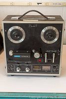 Front view of Akai 1721L reel to reel tape recorder showing dual reels, control knobs, switches, VU meters, and carrying handle on top.