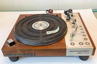 Front and left-side view showing wood-effect plinth, direct-drive platter with mat and tonearm