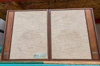 Pair of vintage Ampex speakers showing rectangular wood veneer cases with beige fabric speaker covers, placed side by side.