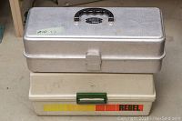 Photo showing two closed tackle boxes stacked, the top metal and the bottom plastic Rebel branded box.