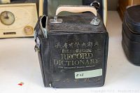 Torn and worn black zippered carrying case with handle and gold text reading English Cantonese Record Dictionary (with International Phonetic Alphabet). Visible wear and tear on the material.