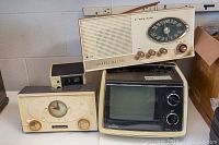 Four vintage items: Sony portable TV at front right, Fleetwood clock radio on top, Hitachi clock radio behind TV, Westclox clock radio at front left.