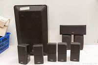 Front view of Bose satellite speakers and Polk Audio speakers with ADS subwoofer in background. Shows relative sizes and condition.