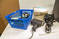 Overview of vintage 8mm movie cameras and lighting including GAF XL Sound, Bell & Howell 375 Filmosound, Polaroid Super Shooter camera in blue basket, two Smith Victor lights, and Bell & Howell camera box.