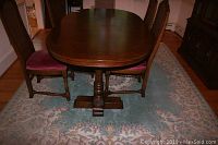 Dining table front view with two chairs showing the wood details and oval shape.