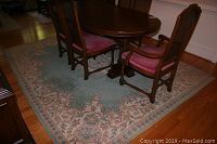 Full view of the area rug under a dining table with wooden floor visible around it.