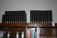 Full view of the 30 leather bound classical music books arranged on a wooden shelf, showing spines with titles and dates.