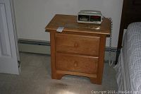 Wooden nightstand on carpeted floor, showing two drawers with round knobs and general wear on the surface.