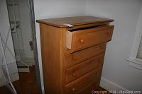 Side and front view of a wooden dresser showing five drawers with round knobs and the top drawer open and needing repair.