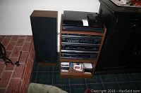 Panasonic stereo system tower with turntable on top, cassette deck, tuner components, and wooden stand with an additional shelf containing CDs and tapes.