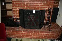 Photo shows a set of black metal fireplace items including a three-panel fire screen with leaf and candle holder details, log holder, and a stand with decorative handles on a brick hearth.