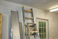 Two aluminum ladders standing in a garage with some other items visible but unrelated to the lot.
