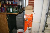 Electric weed trimmer standing upright near a workbench and an orange box with product details.