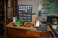 Full view of the workbench with the scroll saw placed next to a storage organizer and some gloves and fasteners.