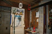 Full view of corner with metal shelf, hand tools on brown pegboard including hammer and screwdrivers, hanging fishing nets, and two suspended lanterns.