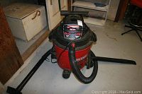 Front side view of the red and black Craftsman wet/dry vacuum with hose and attachments arranged around base on floor.