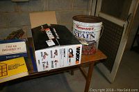 Photo of the lot's items on a table showing the Worx chainsaw box, first aid kit, and metal bucket with fishing items.
