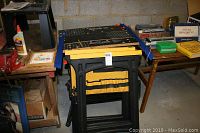 Two folded Black and Decker Workmate 550 saw horses standing side by side in a basement setting among other stored items.