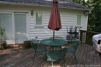 Full view of green metal round patio table with four matching chairs, red umbrella, and concrete umbrella stand on wood deck.